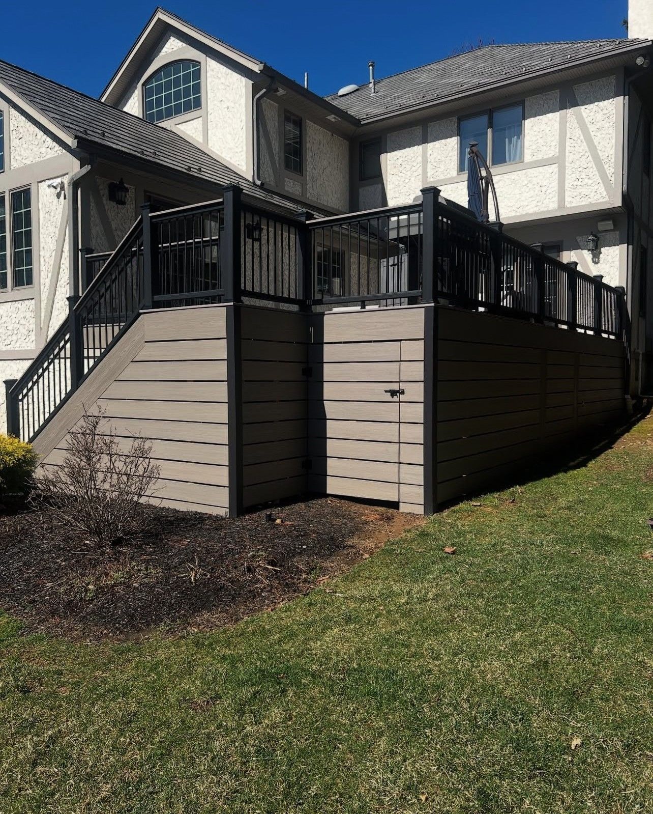 Composite deck with black railing attached to a two-story house, tan siding, and grass.