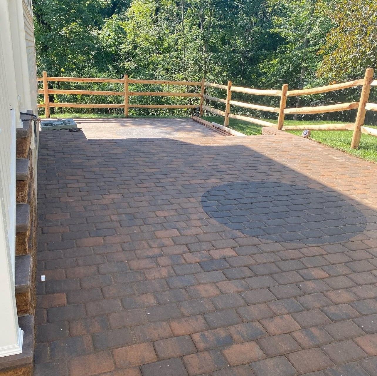 Brick patio with wooden fence and trees in background.