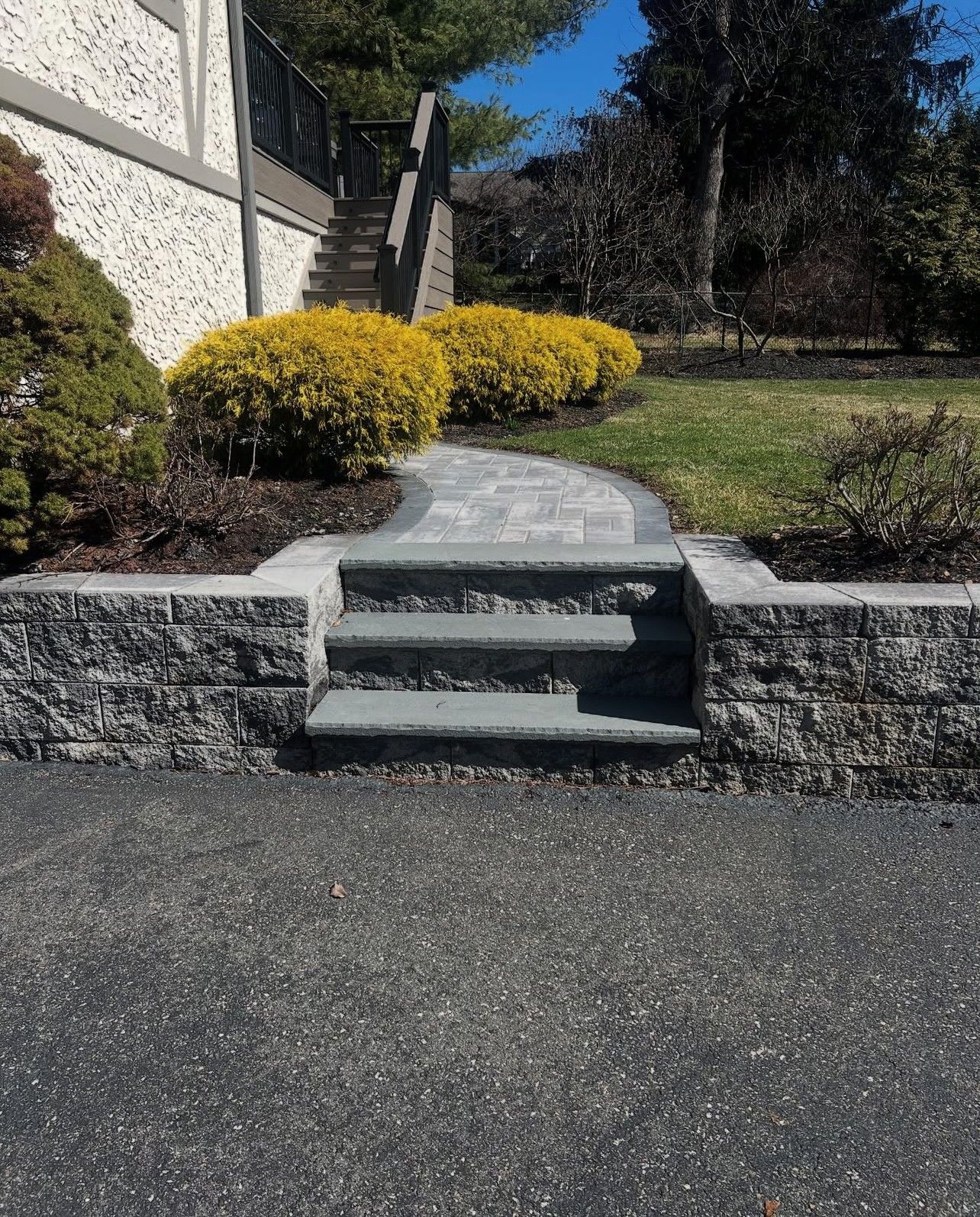 Stone steps and walkway leading uphill, flanked by retaining walls and landscaping. Sunny day.