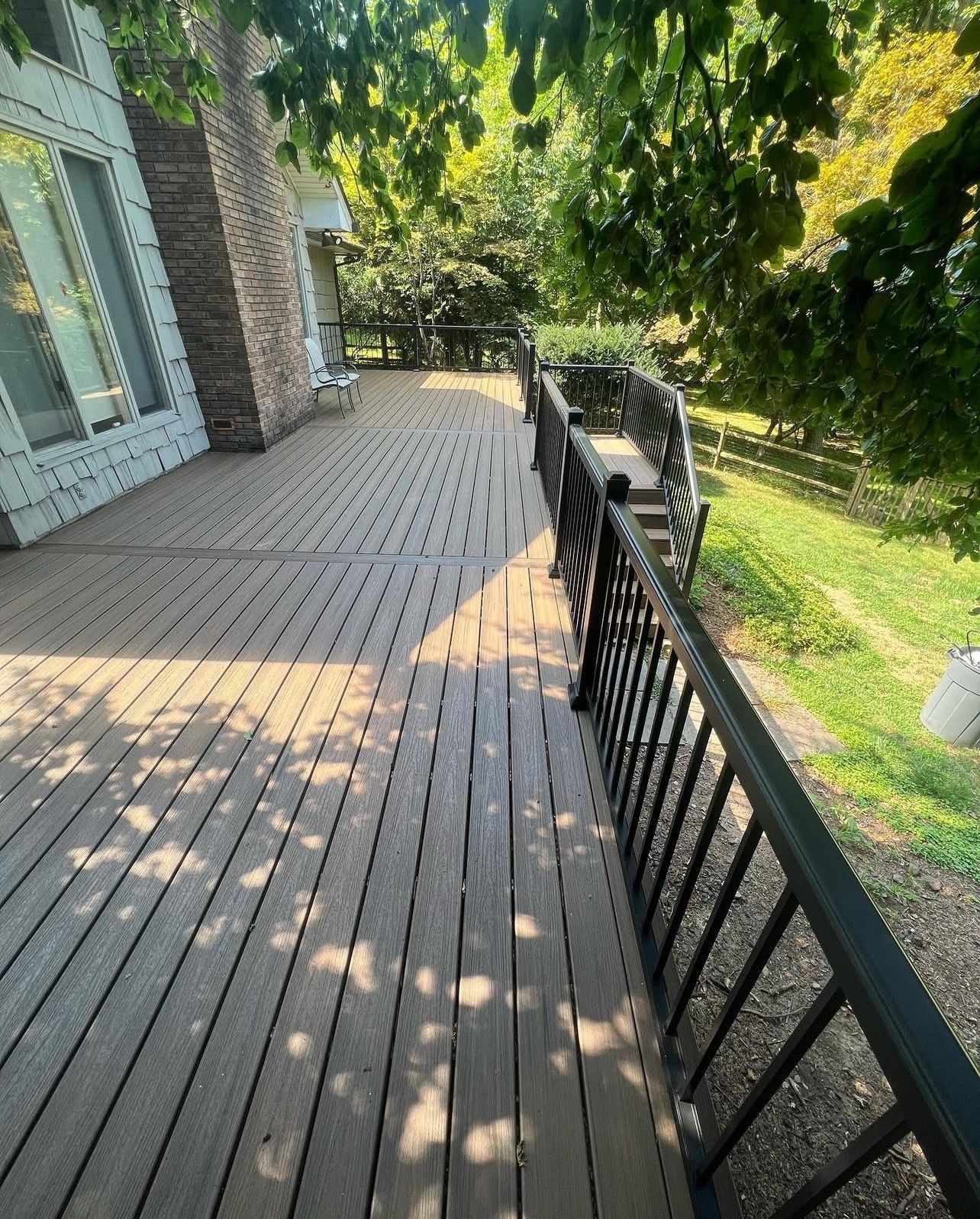 Wooden deck with black railing and lush green trees.