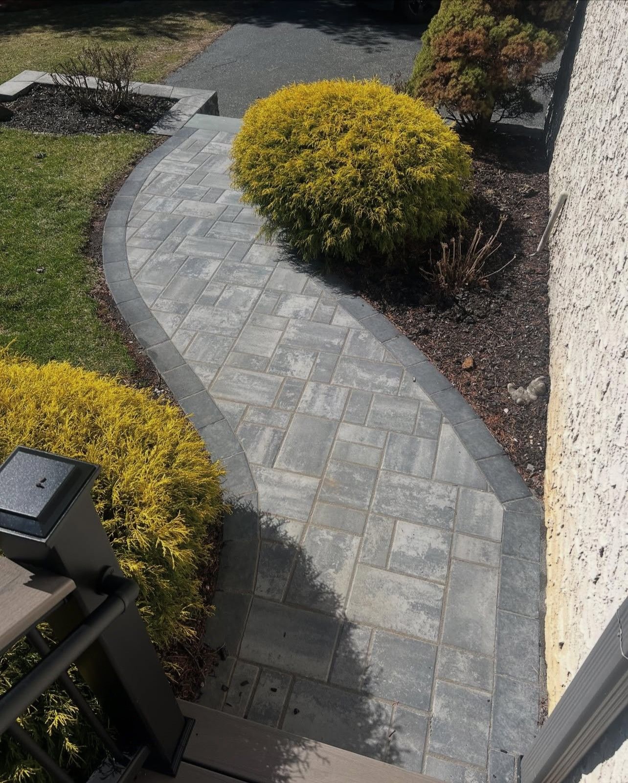 Brick pathway curves through a yard, bordered by bushes and grass.