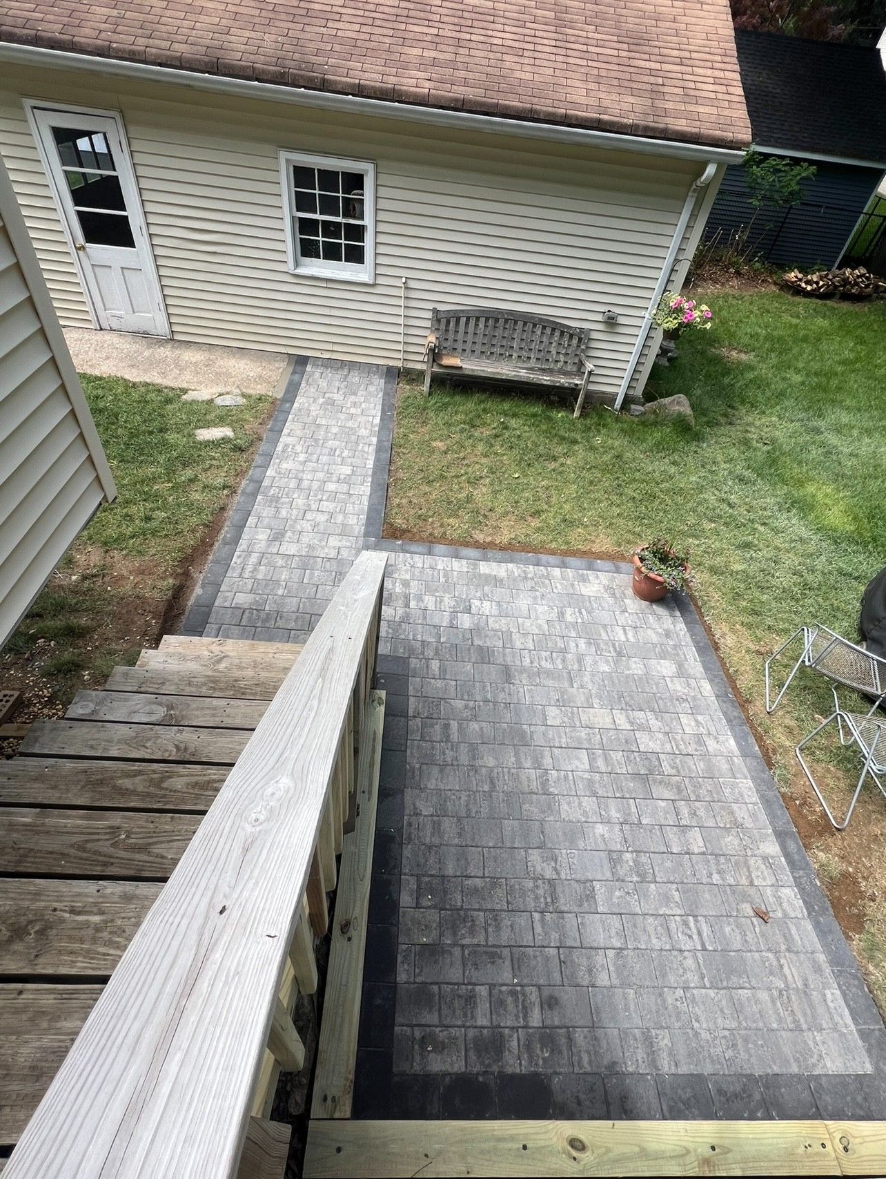 A brick pathway leading to a garage with a bench, viewed from wooden stairs.
