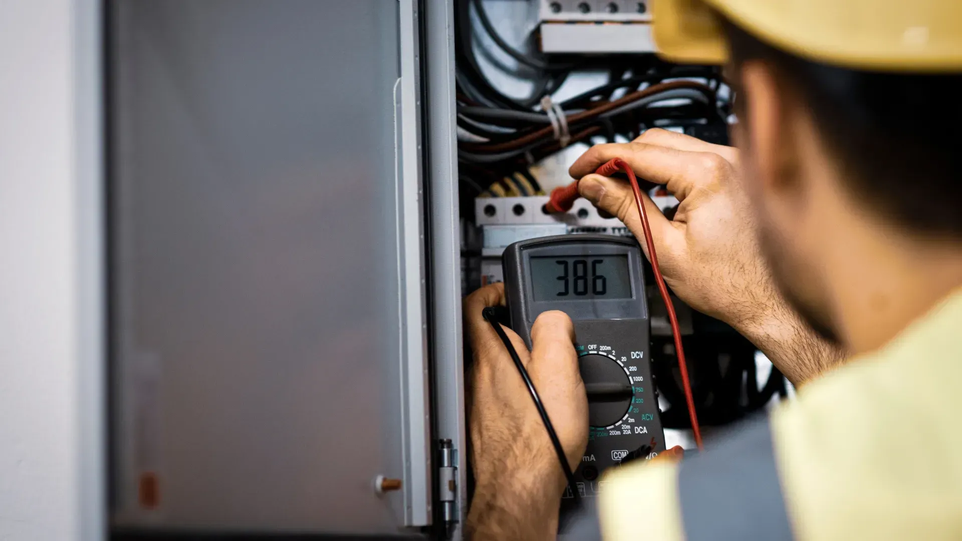 An electrician is using a multimeter to test an electrical box.
