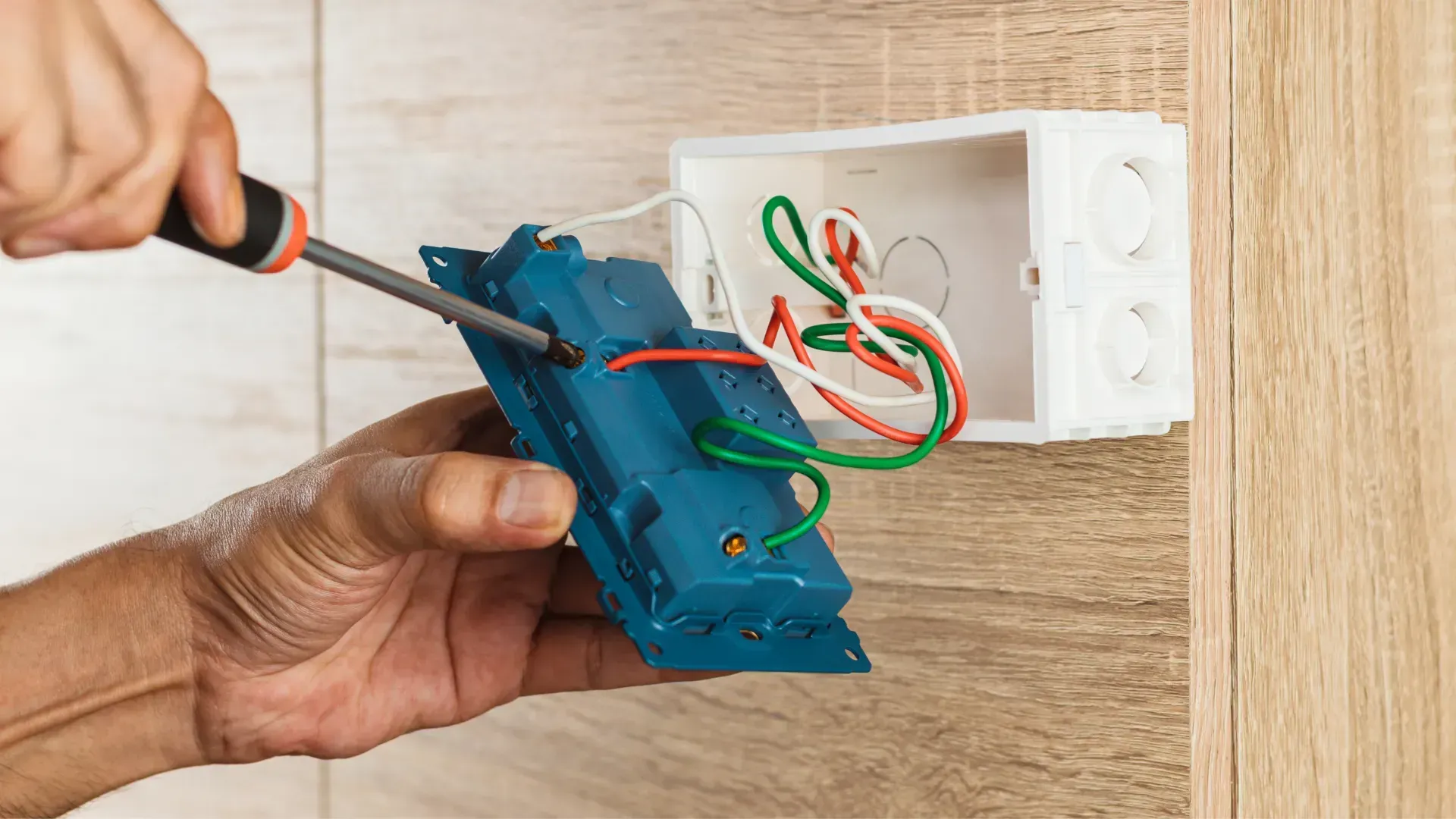 A person is fixing a light switch with a screwdriver.