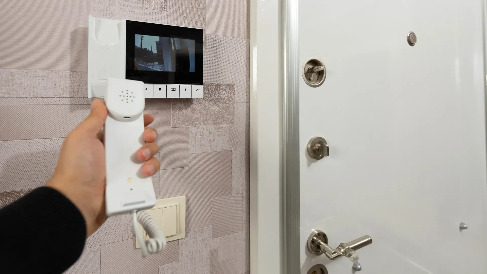 A person is holding a video doorbell in front of a door.