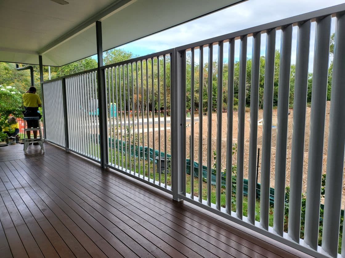 A Man is Standing on a Ladder on a Balcony With a White Railing — A & B Lattice World & Patios In Cassowary Coast, QLD