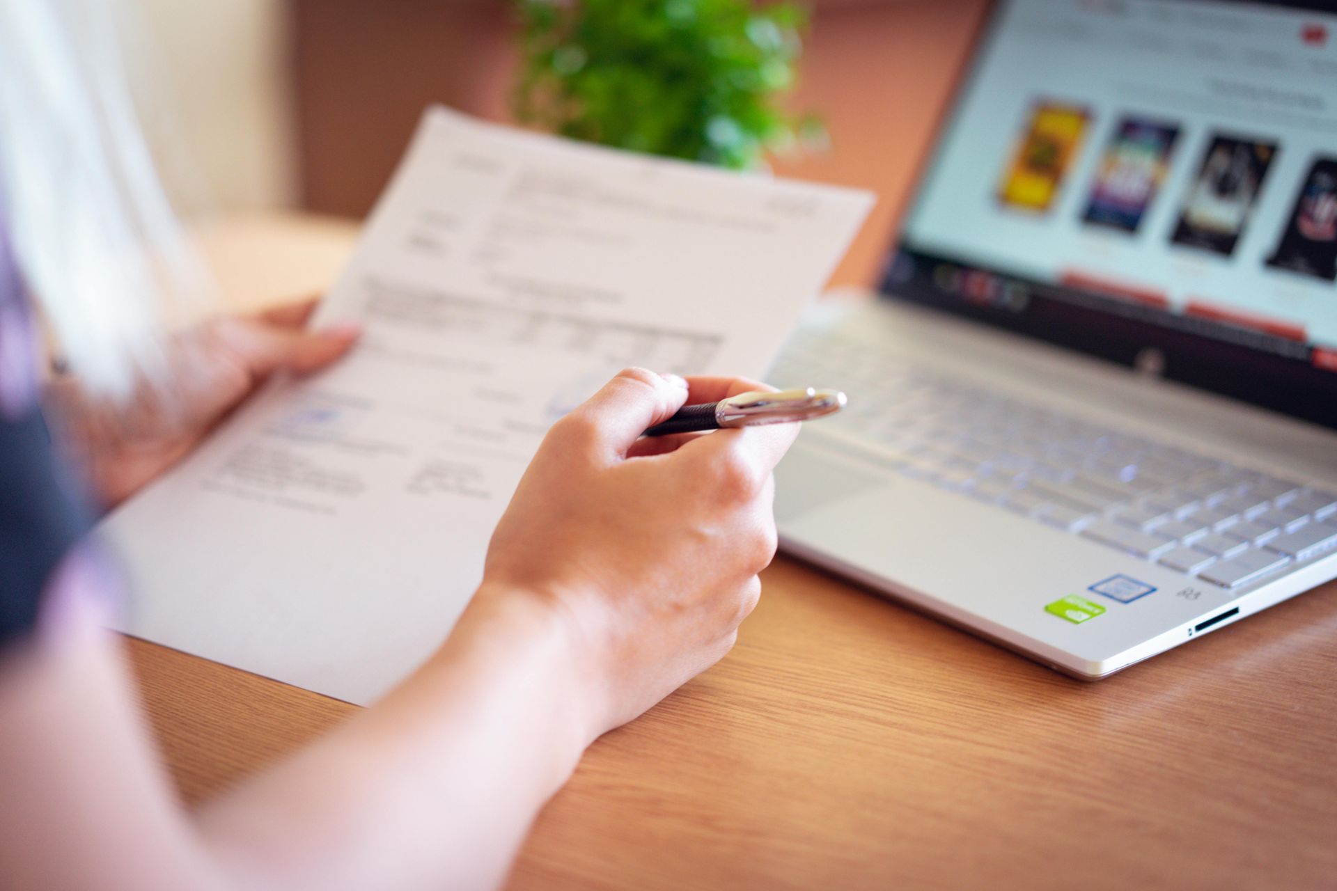 Person sitting at desk, holding paper and pen, with laptop open.