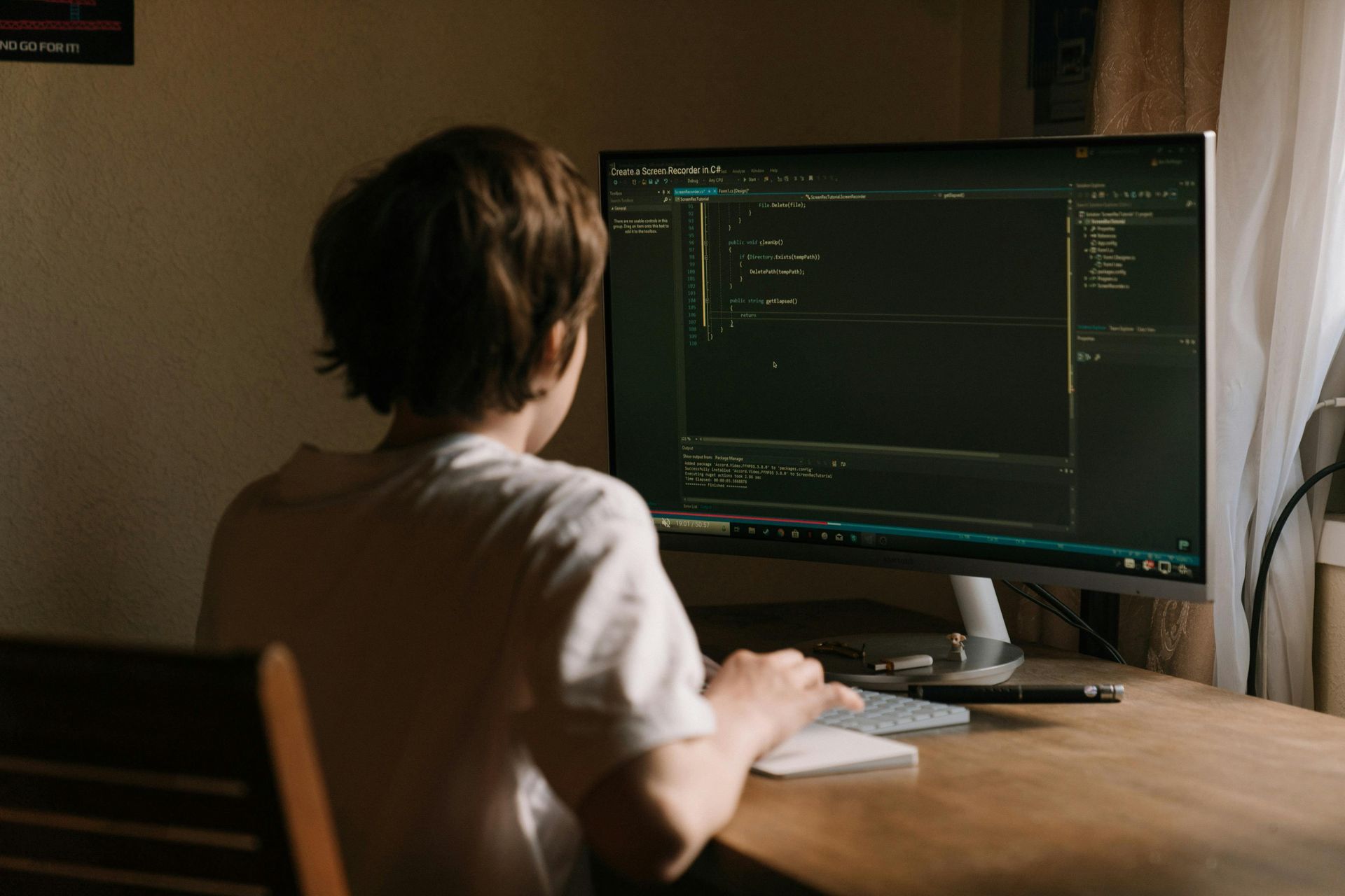 Person sitting at a desk, coding on a computer with a large monitor.