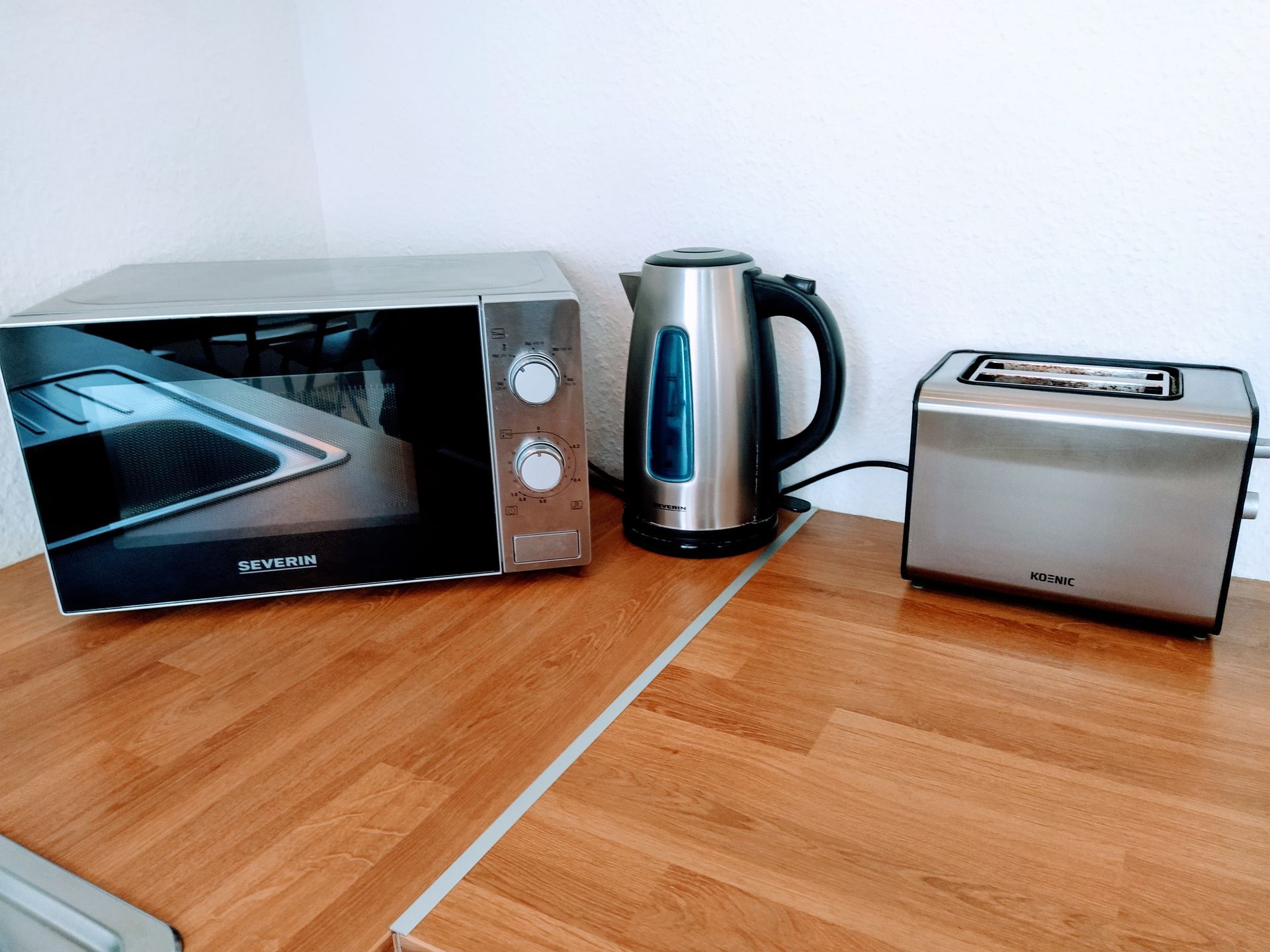 A microwave , kettle and toaster are on a wooden counter in our Berlin vacation apartment.