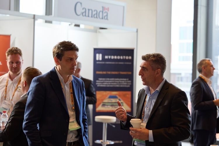 Two men in suits converse at a trade show booth; 