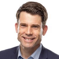 Man in a blue suit smiles at the camera against a white backdrop.