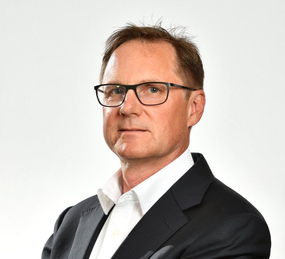 Woman with blonde hair wearing a black blazer smiles at the camera.