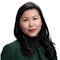 Woman with dark hair smiles, wearing a black sweater over a white collared shirt.