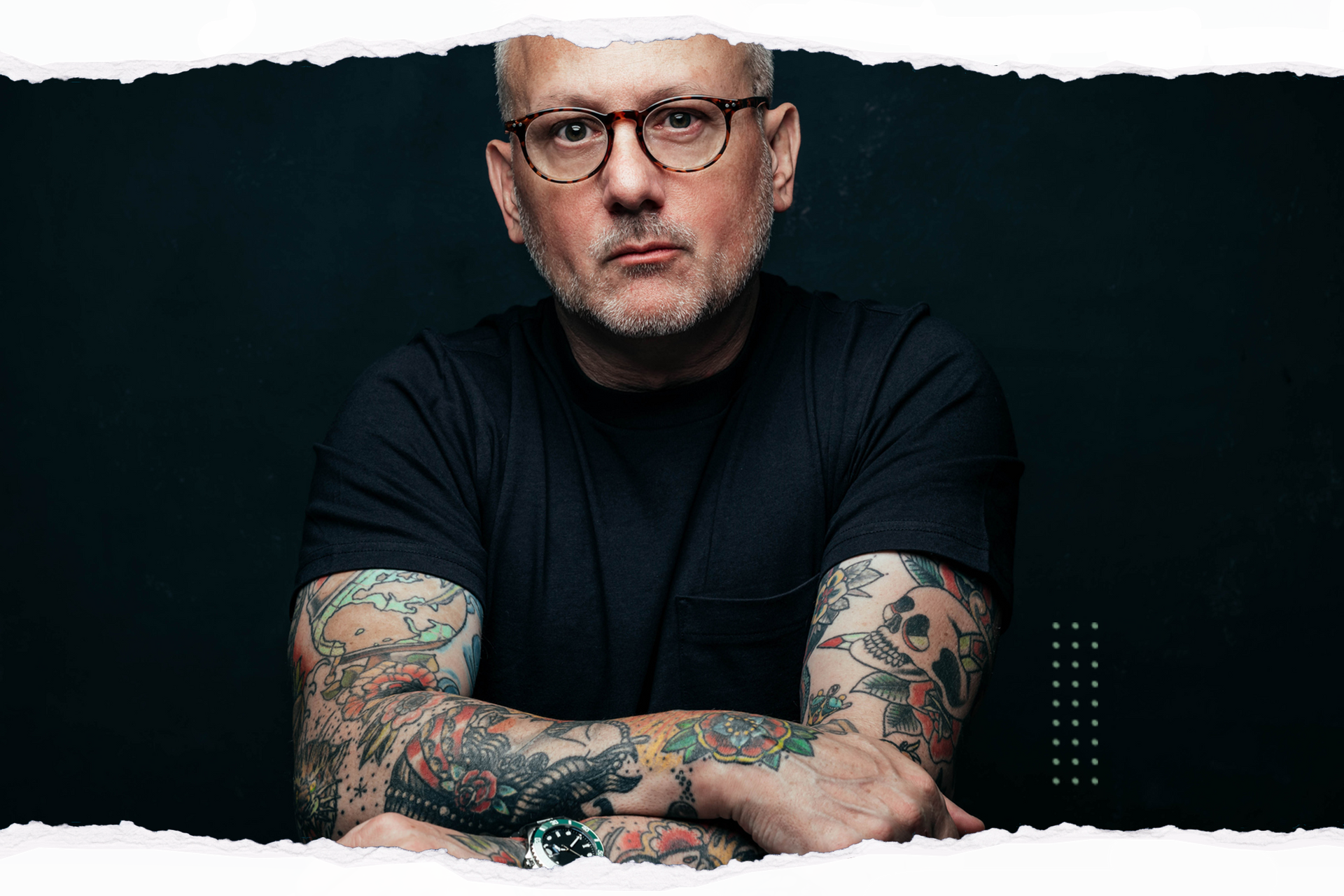 The man is wearing glasses and has a lot of tattoos on his arms.