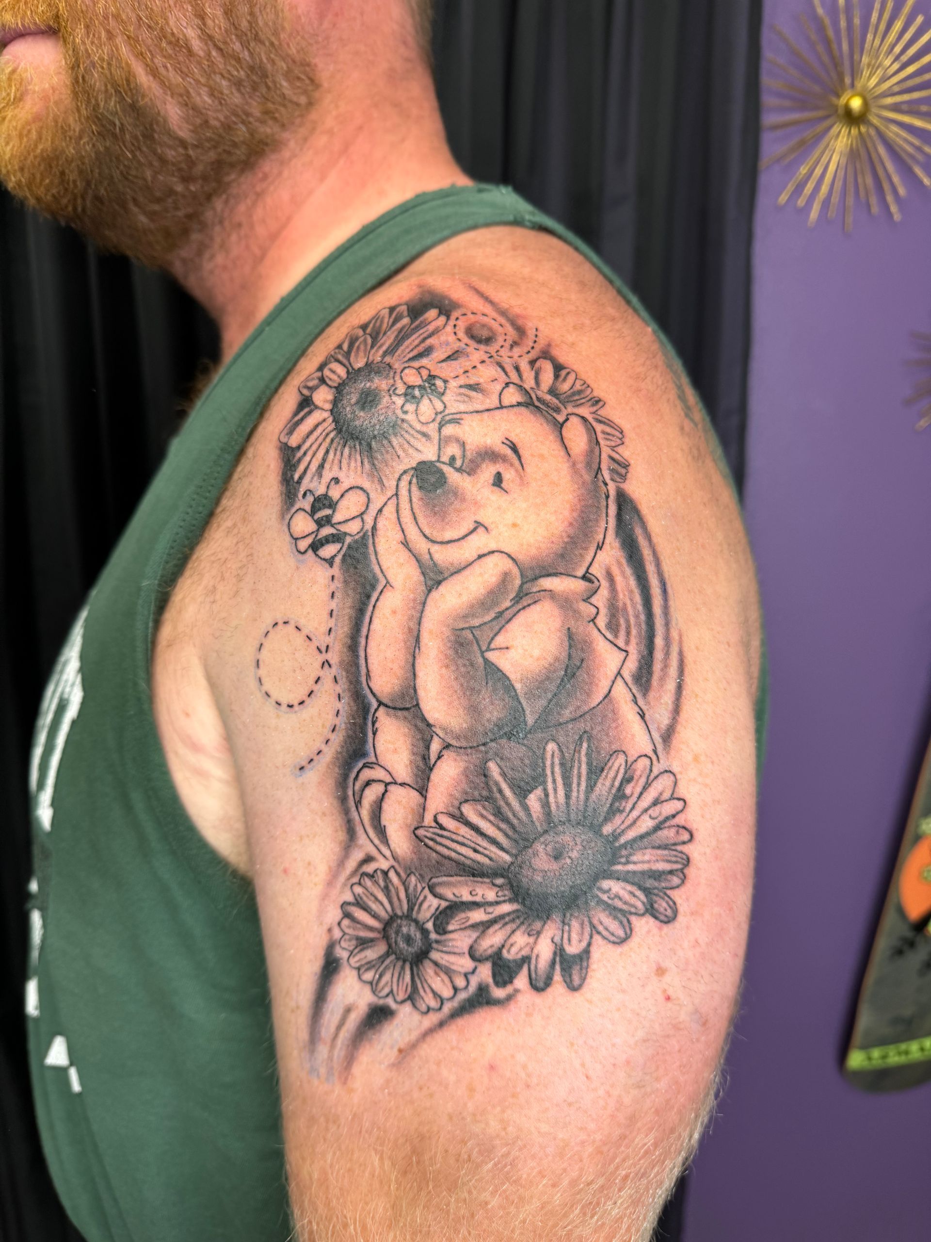 A man with a beard and tattoos on his arms is sitting on the floor with his hands folded.