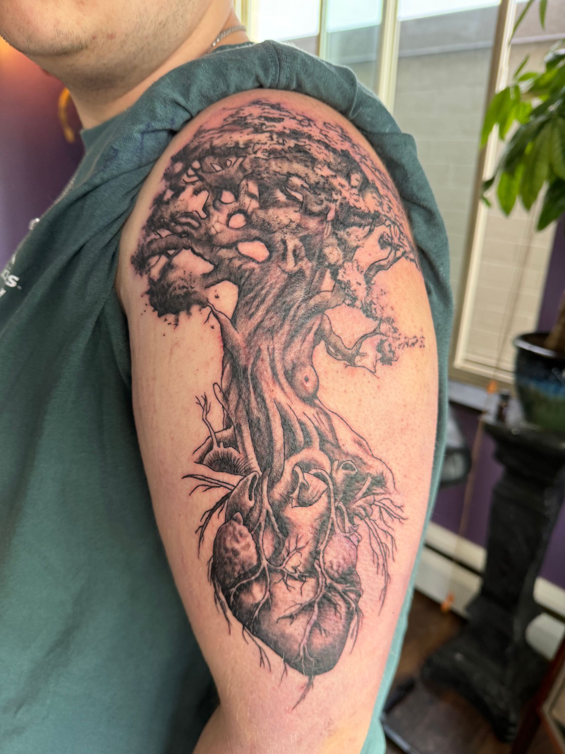 A woman with tattoos on her arms is standing in front of a brown wall.