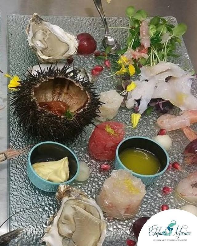 Un piatto di vetro con un assortimento di frutti di mare crudi, tra cui ostriche