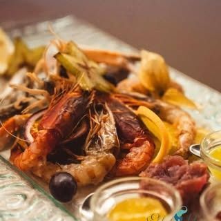 Su un tavolo, un piatto con gamberi cotti, fette di carambola, un acino d'uva scura e ciotoline con salse per intingere.