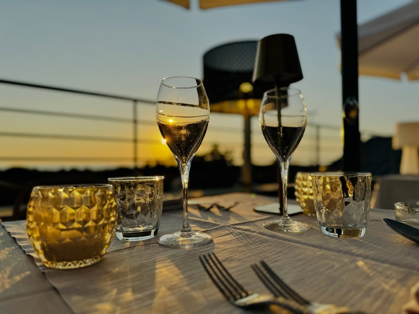 Due calici da vino e piccoli portacandele su un tavolo apparecchiato per una cena all'aperto al tramonto