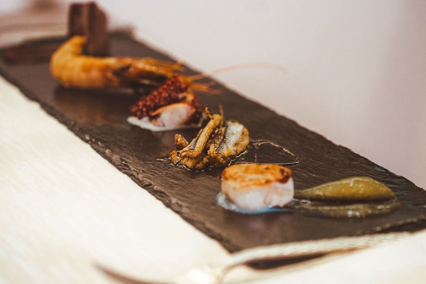 Su un vassoio di ardesia è disposta una fila di piccoli antipasti di pesce, tra cui un gambero