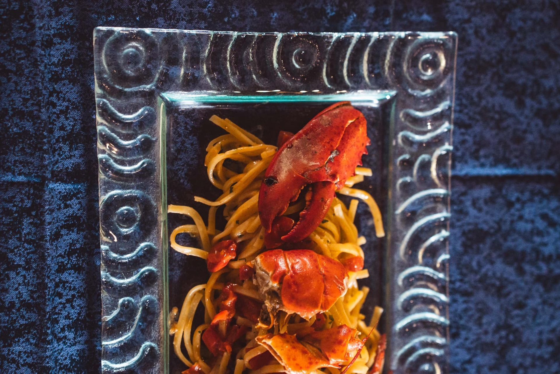 Una chela di aragosta e pezzi di polpa di aragosta serviti su linguine in un piatto di vetro decorato