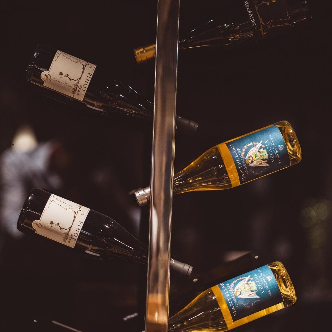 Una rastrelliera per vini contiene diverse bottiglie di vino rosso e bianco, esposte inclinate su uno sfondo scuro.