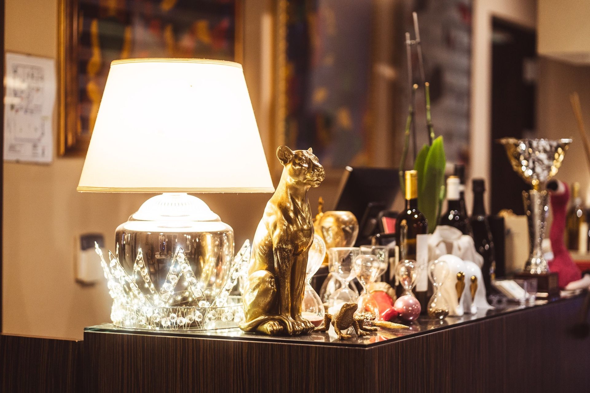 Una lampada da tavolo accesa, una statuetta di gatto dorata e vari oggetti decorativi disposti su un bancone scuro e lucido.