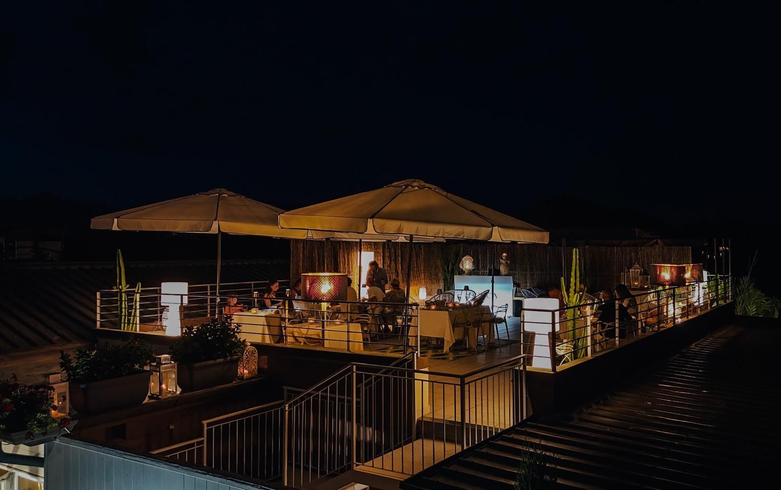 Di sera, una terrazza sul tetto con tavoli, sedie, ombrelloni e luci soffuse crea un invitante spazio per cenare all'aperto.