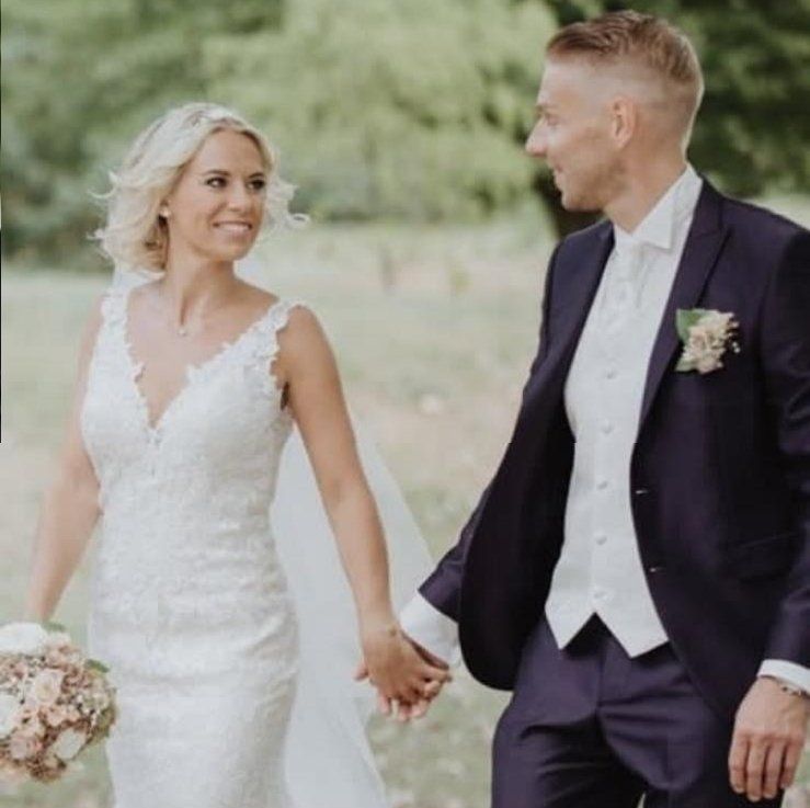 Eine Braut und ein Bräutigam halten Händchen, während sie auf einem Feld spazieren gehen