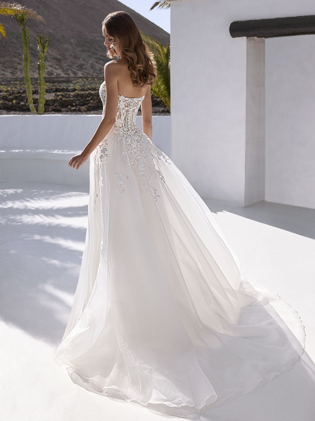 Frau in einem trägerlosen weißen Brautkleid mit langer Schleppe geht im Freien spazieren.