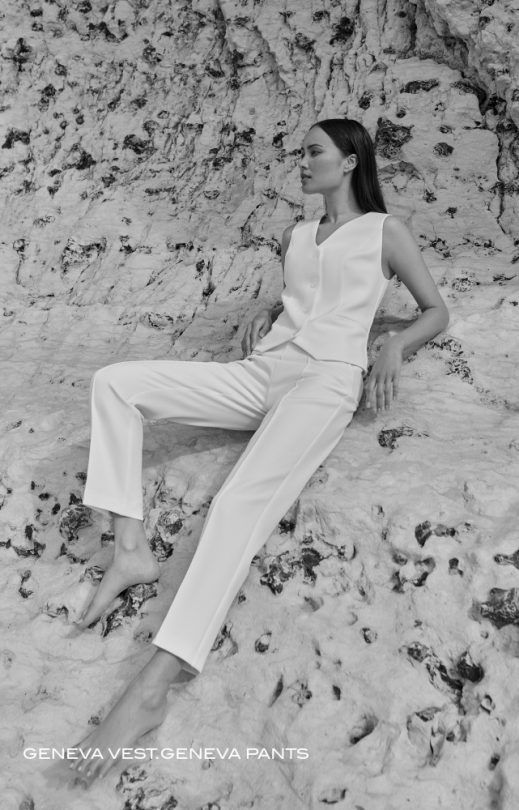 Eine Frau in einem weißen Overall sitzt im Sand.