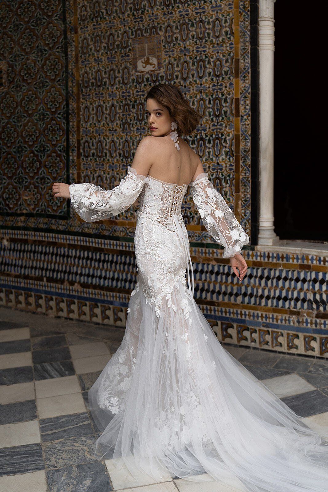 Eine Frau in einem weißen Brautkleid steht vor einer gefliesten Wand.