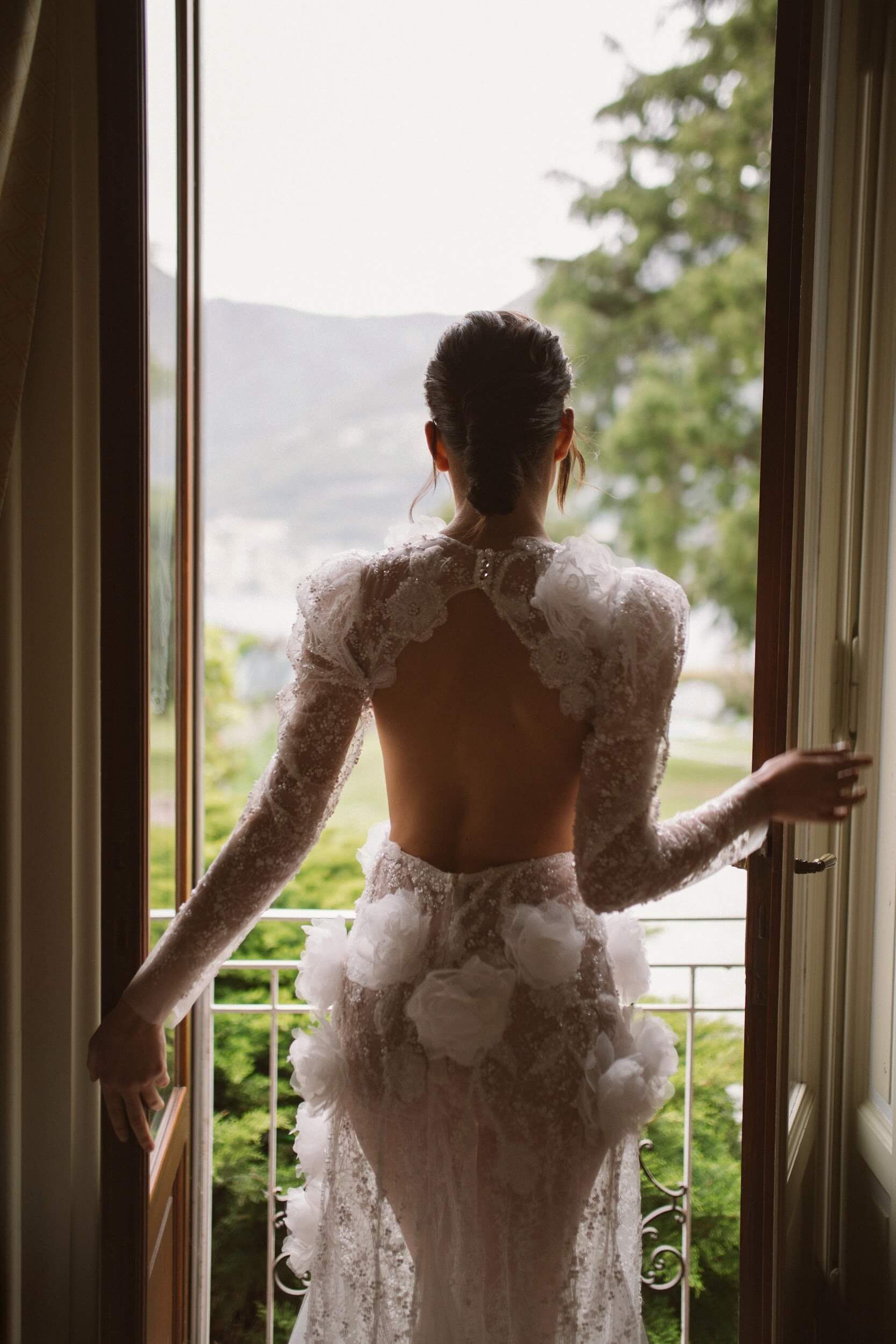 Eine Frau in einem Brautkleid steht vor einem Fenster.
