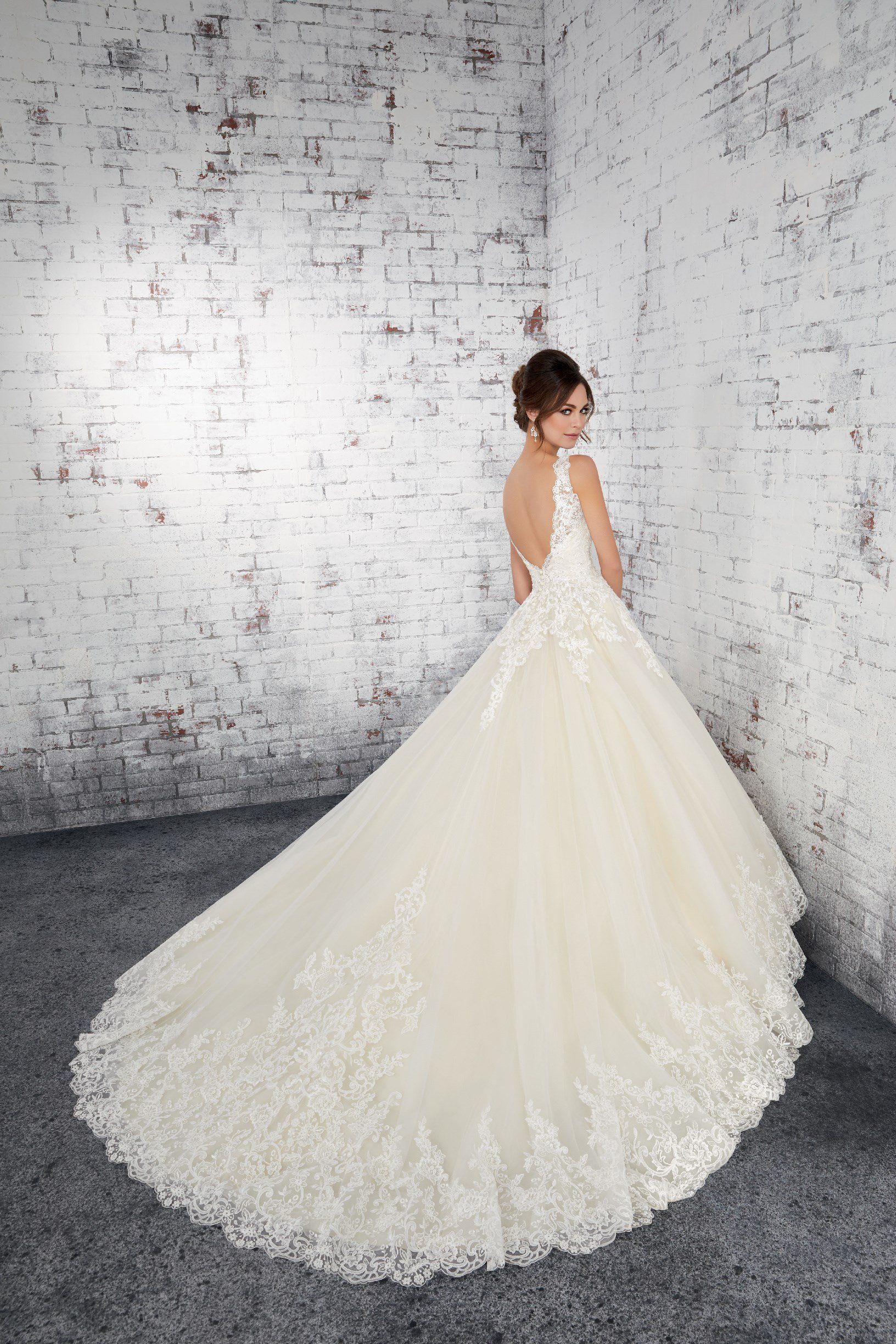 Eine Frau in einem Brautkleid steht vor einer weißen Backsteinmauer.