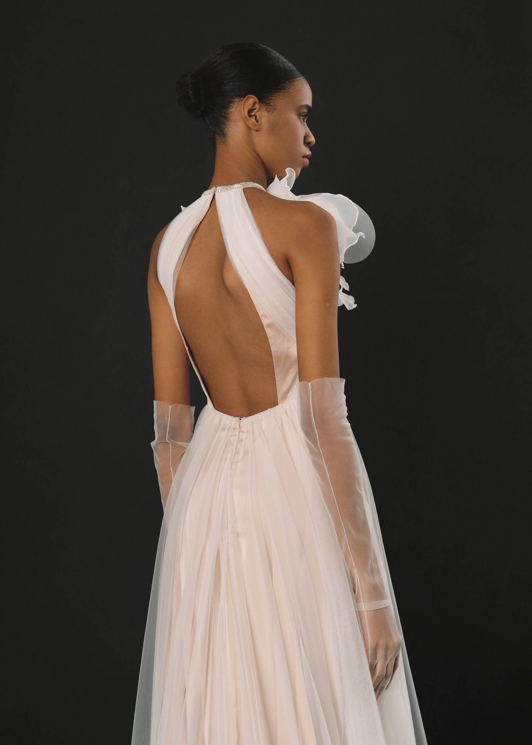 Eine Frau in einem weißen Kleid und Handschuhen steht vor einem schwarzen Hintergrund.