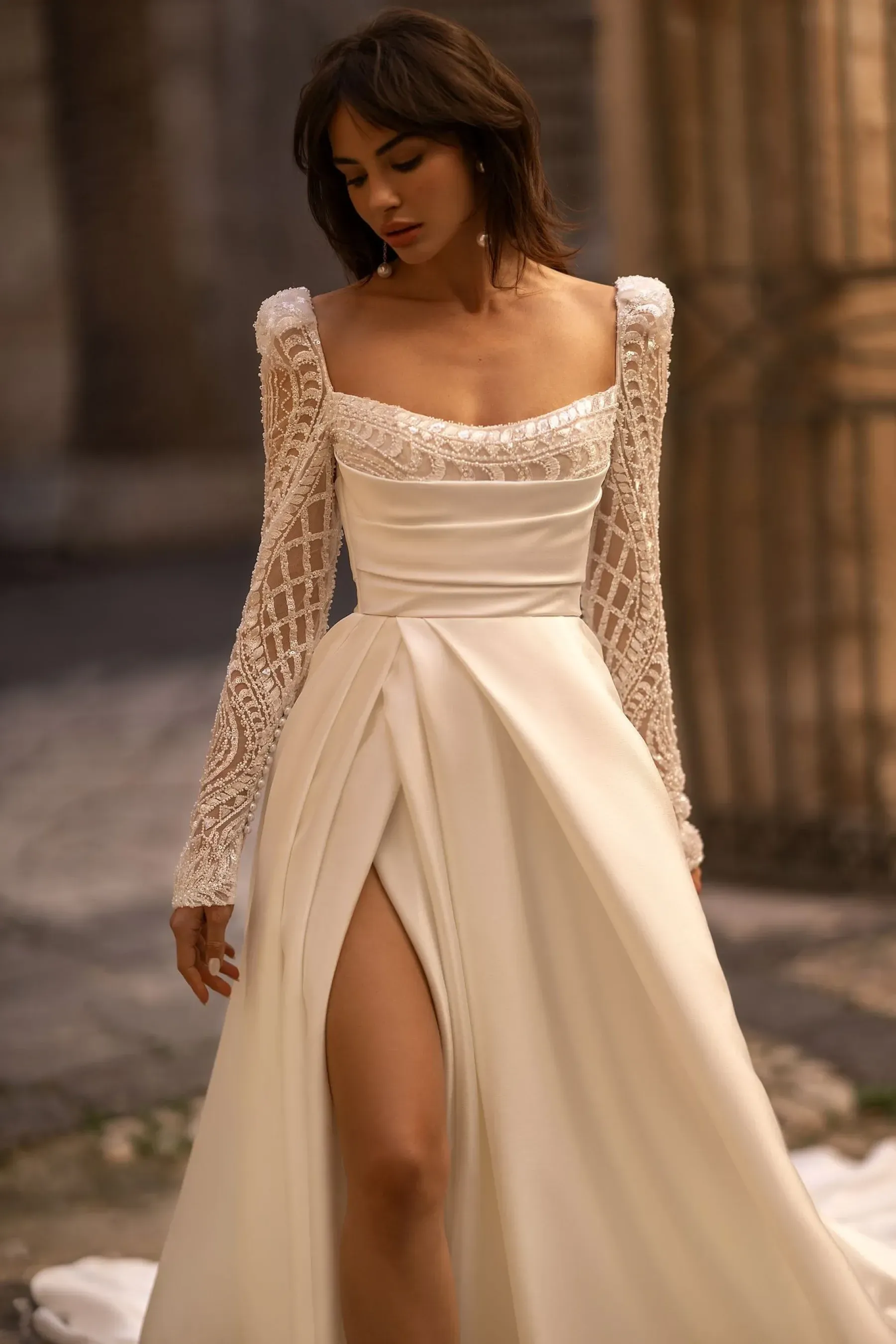 Eine Frau trägt ein weißes Brautkleid mit langen Ärmeln und einem hohen Schlitz.