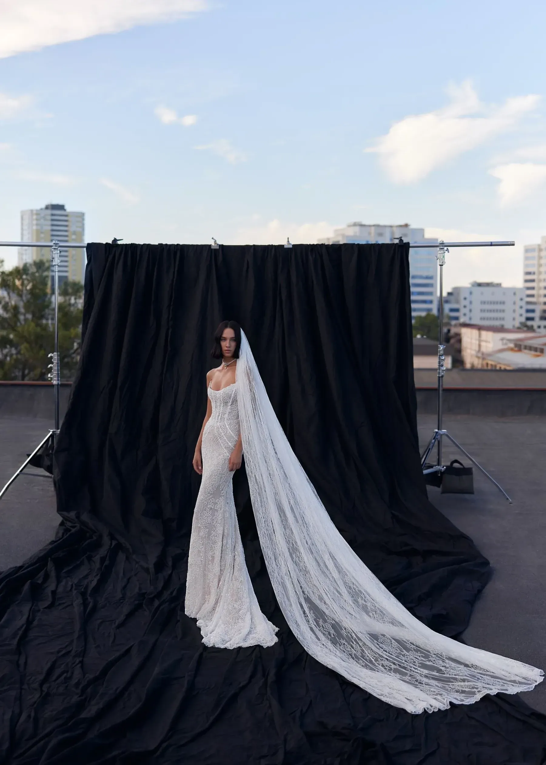 Frau im Brautkleid, langer Schleier, steht vor schwarzem Hintergrund auf einem Dach.