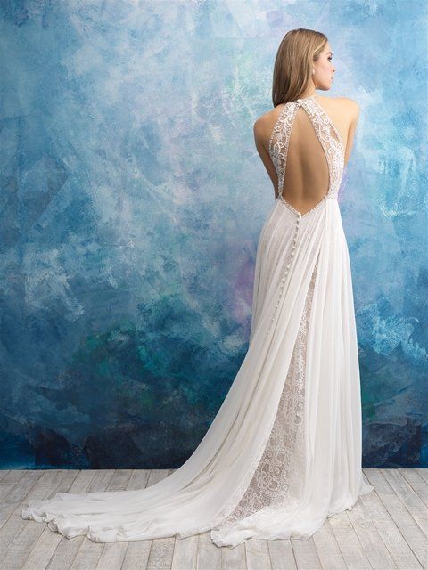 Eine Frau in einem weißen Brautkleid mit tiefem Rückenausschnitt steht vor einer blauen Wand.