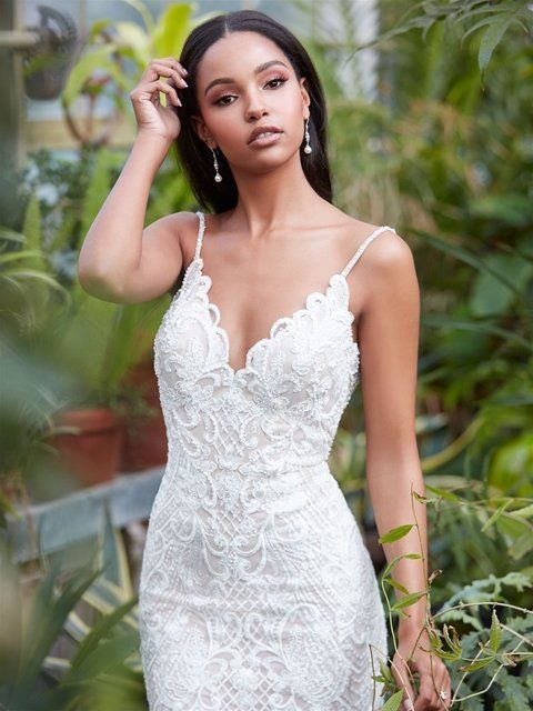 Eine Frau in einem weißen Spitzenkleid steht in einem Gewächshaus.