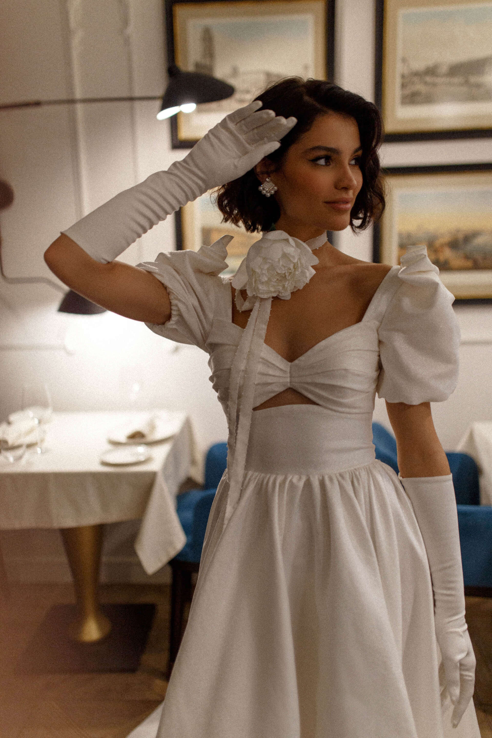 Eine Frau in einem weißen Kleid und weißen Handschuhen steht in einem Restaurant.