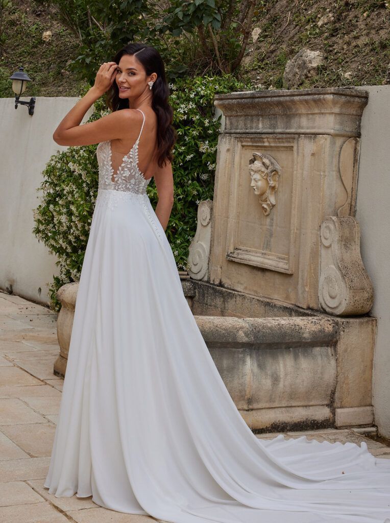 Eine Frau in einem weißen Brautkleid steht vor einem Brunnen.