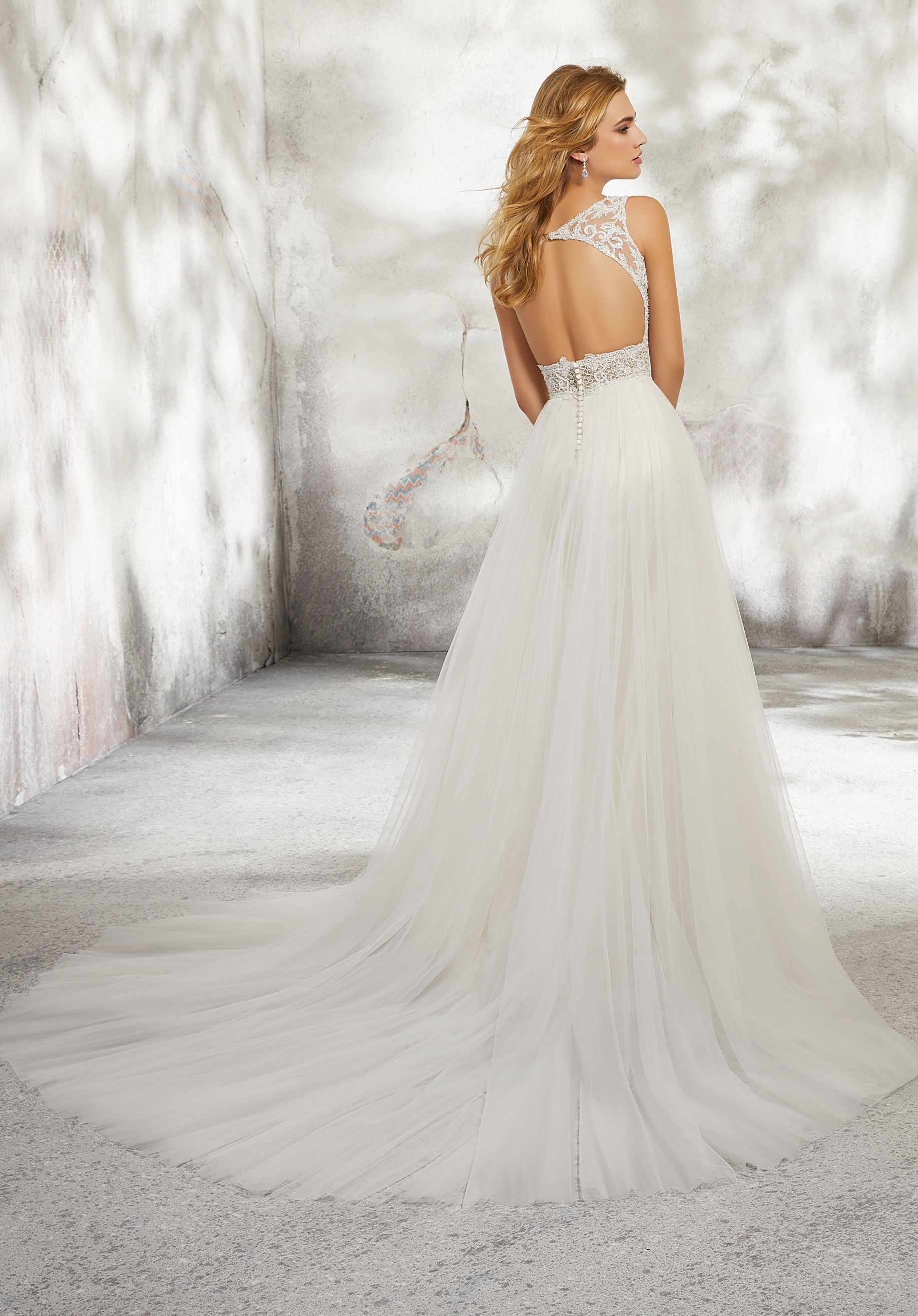 Eine Frau in einem weißen Brautkleid steht vor einer Wand.