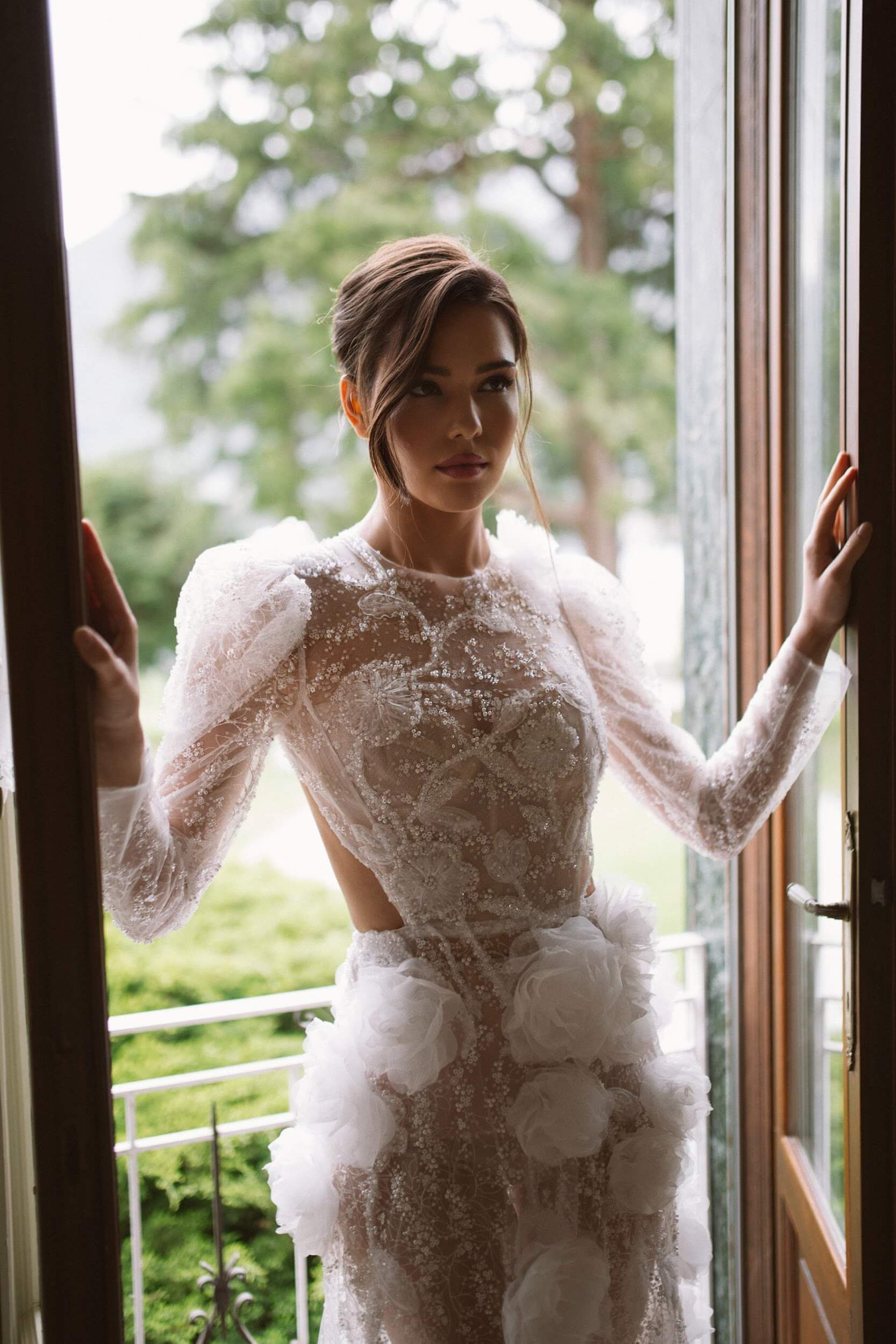 Eine Frau in einem Brautkleid steht vor einem Fenster.