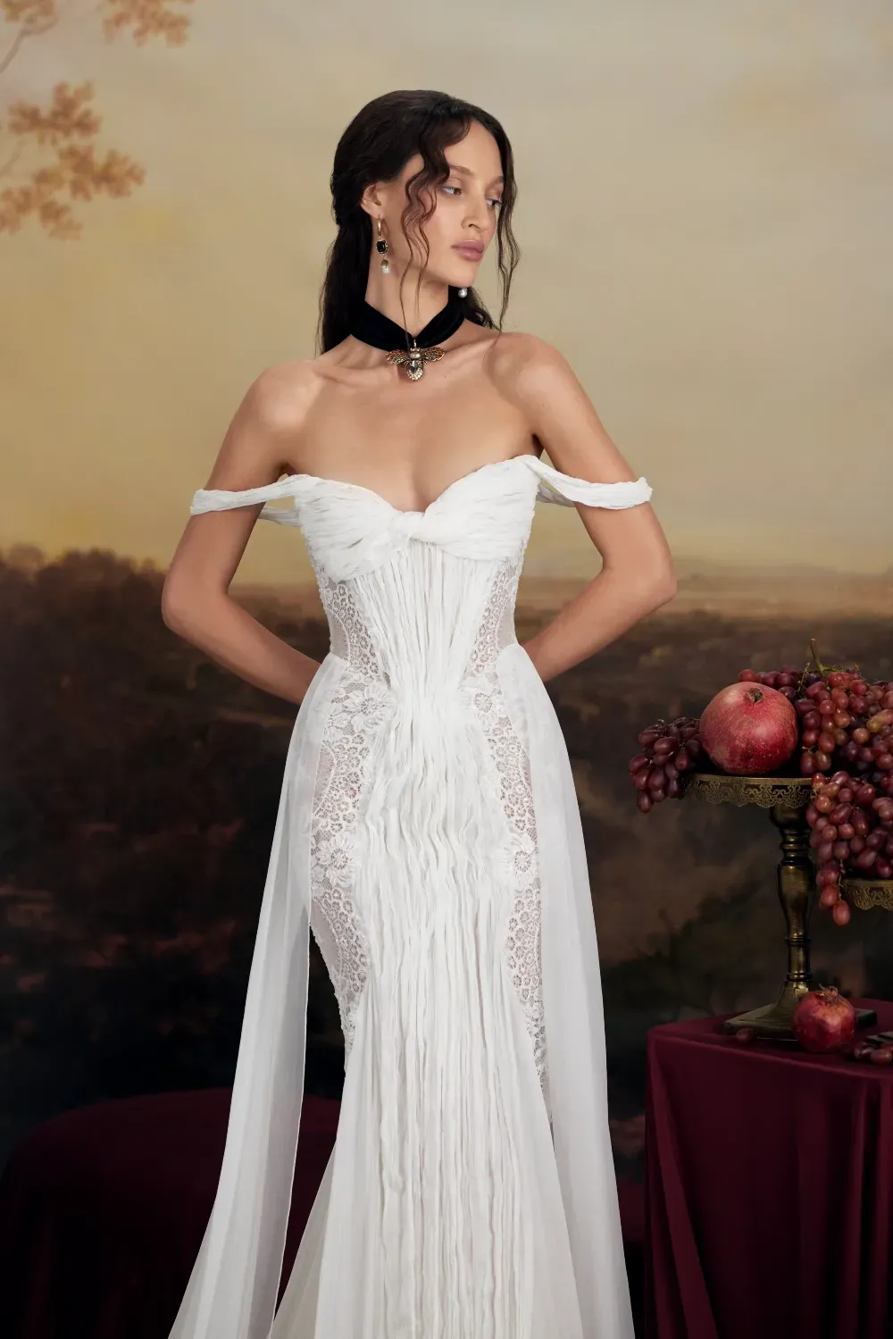 Frau in weißem schulterfreiem Kleid, stehend, in einem klassischen Kunstatelier-Ambiente.