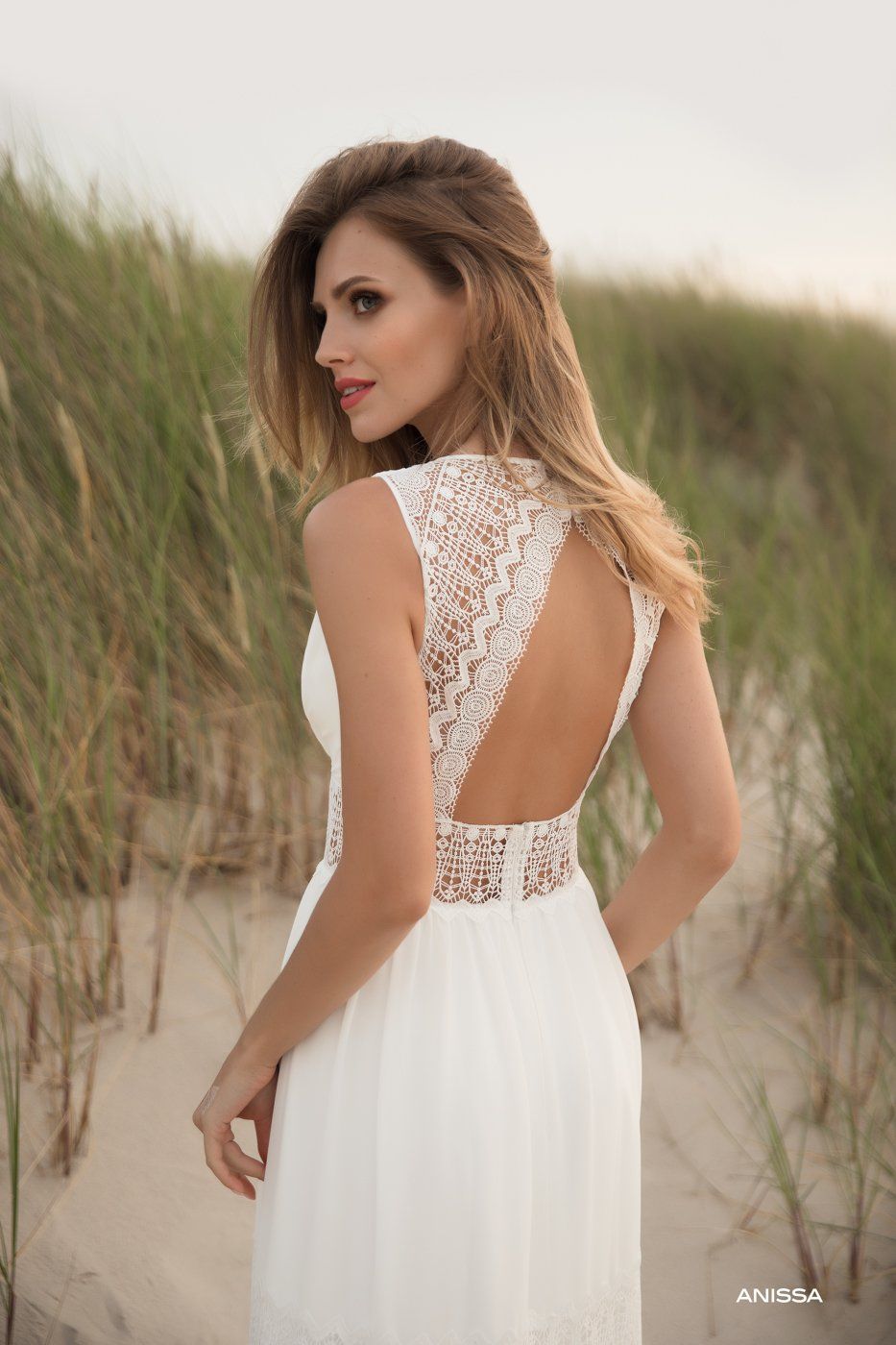 Eine Frau in einem weißen Kleid steht auf einem Feld mit hohem Gras.