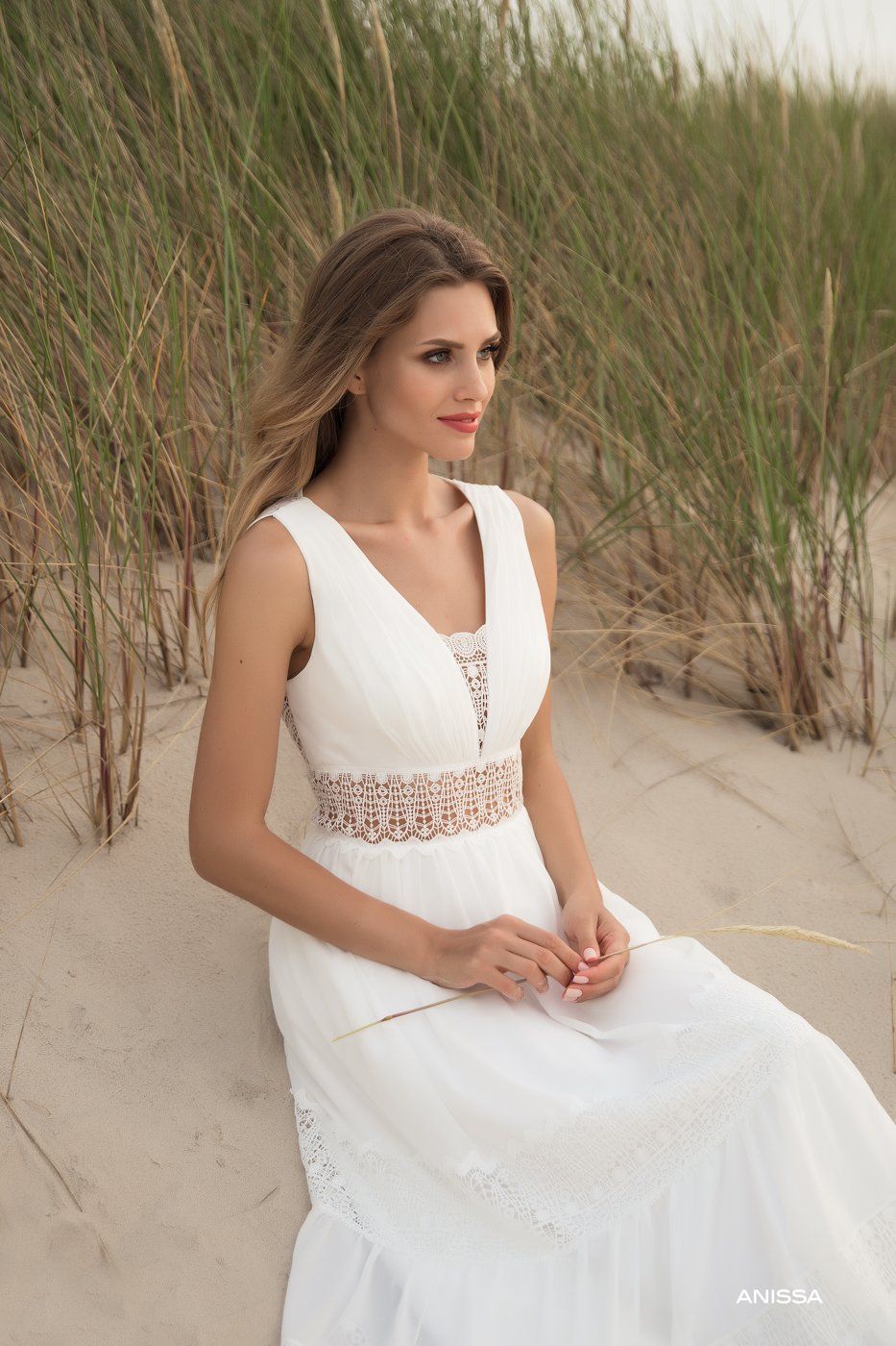 Eine Frau in einem weißen Kleid sitzt auf einer Sanddüne.