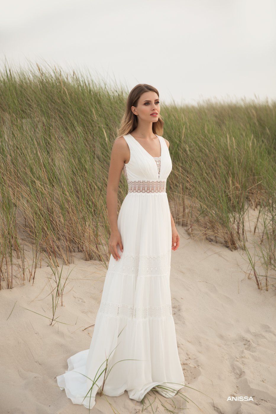 Eine Frau in einem weißen Kleid steht an einem Sandstrand.