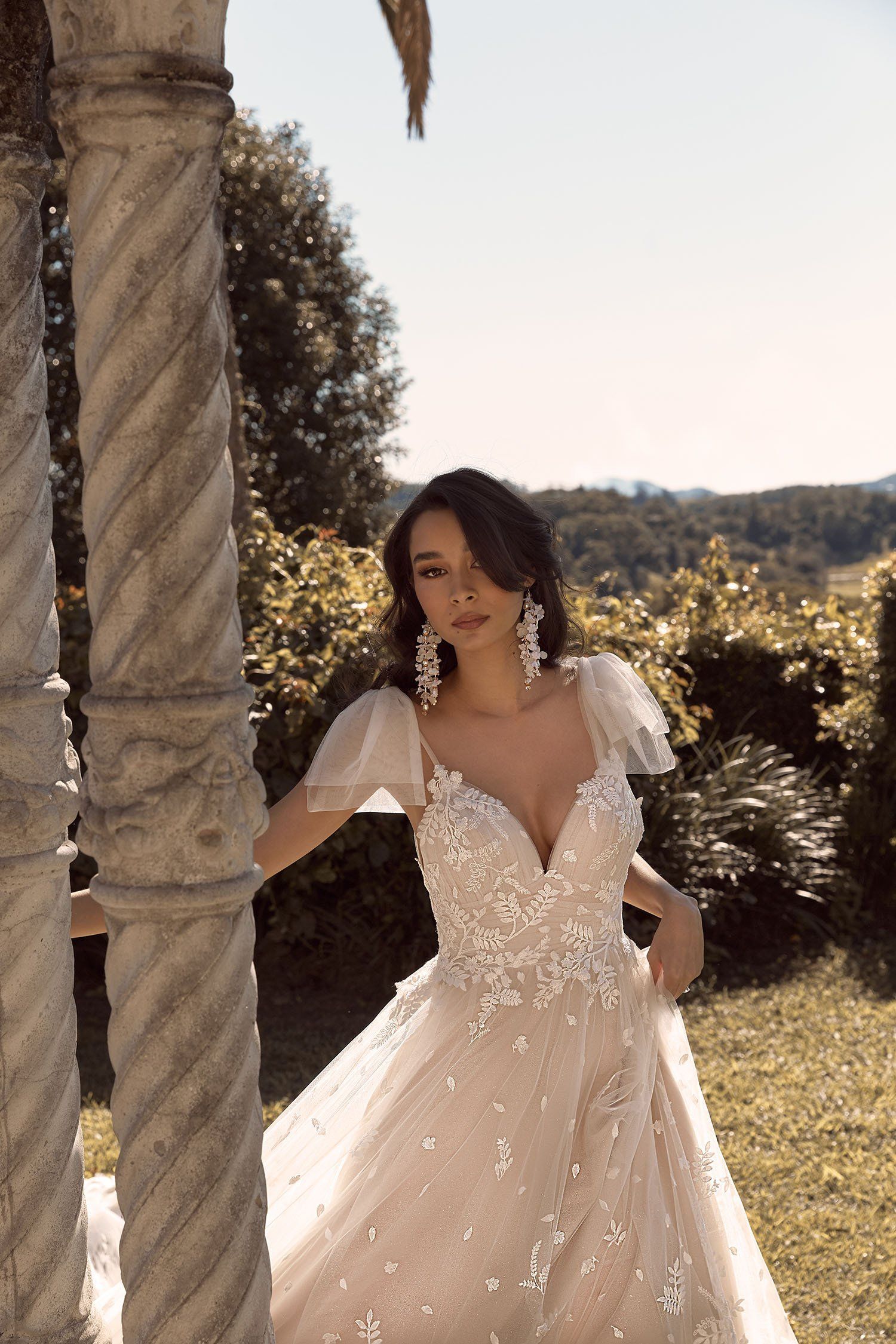 Eine Frau in einem Brautkleid steht neben einer Steinsäule.