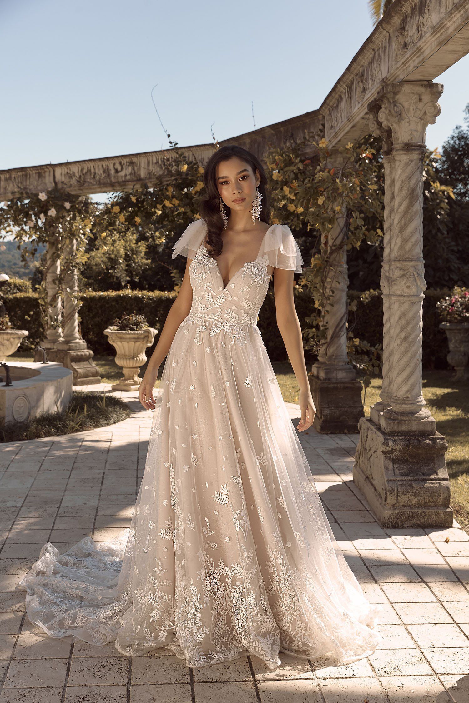 Eine Frau in einem Brautkleid steht vor einem steinernen Torbogen.