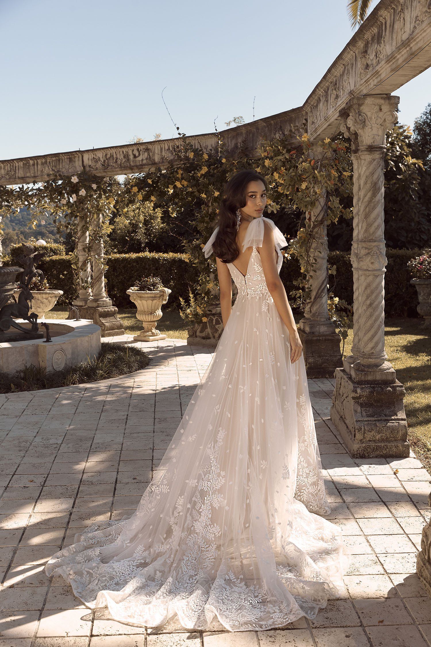 Eine Frau in einem Brautkleid steht vor einem steinernen Torbogen.